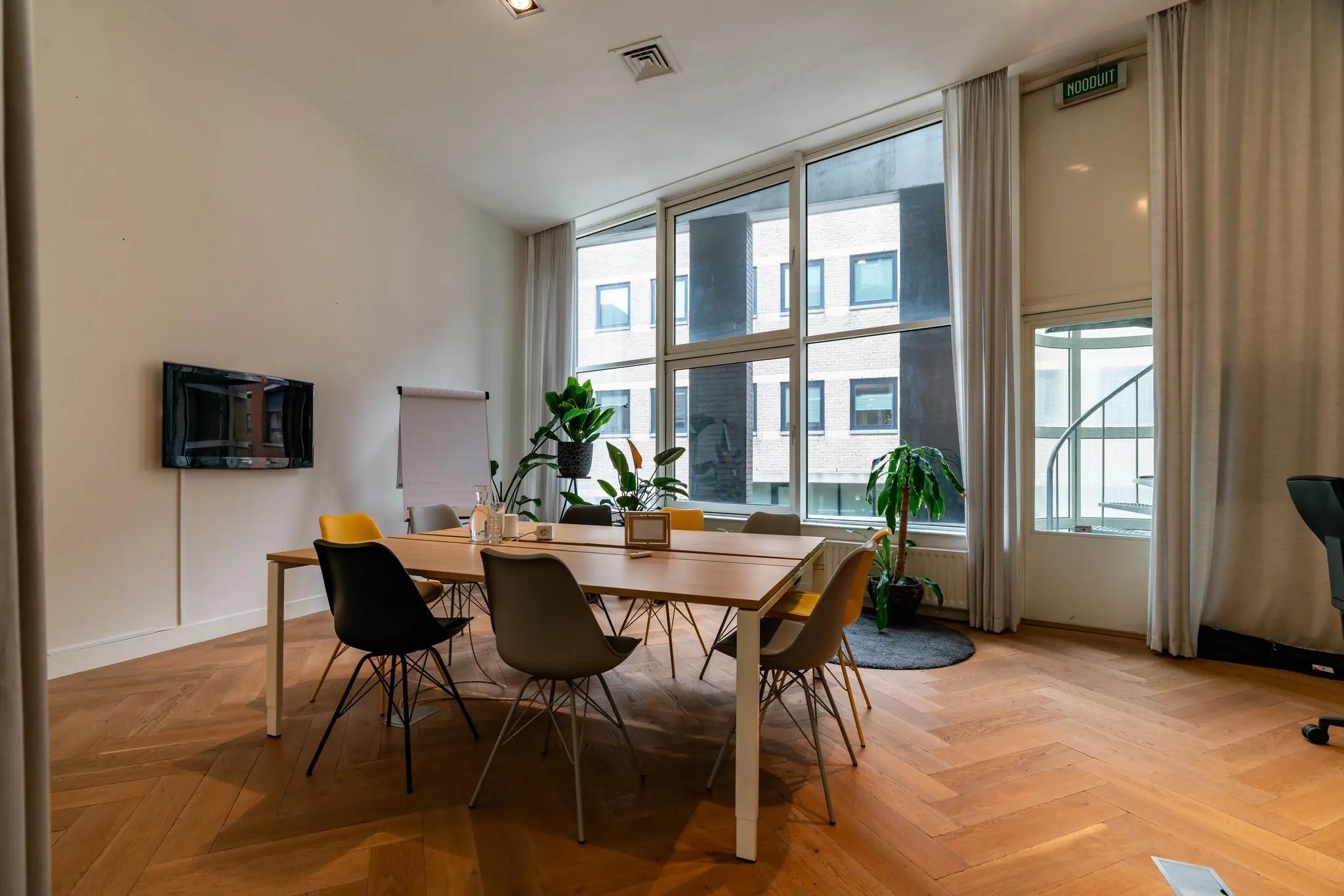 Vergaderruimte aan de Lange Vijverberg met moderne inrichting, grote ramen, planten en een ronde tafel met kleurrijke stoelen.